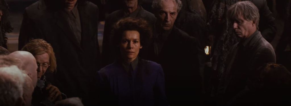 A severe looking white woman in a long sleeved purple dress with her brown hair pinned up stares at Cybil and Rose.